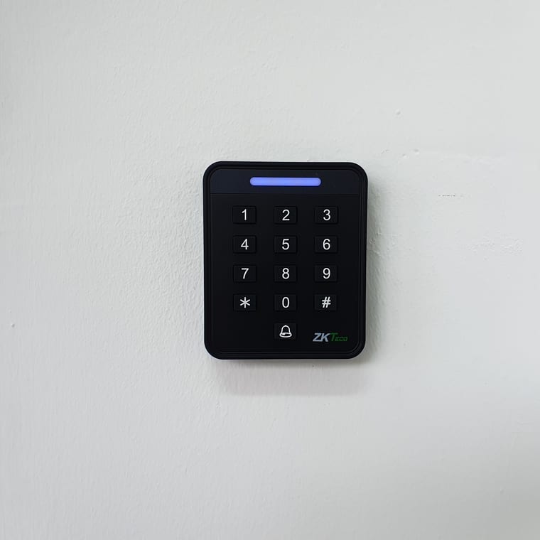 A ZKTeco keypad and RFID door reader with a blue status bar, mounted on a rendered white wall.