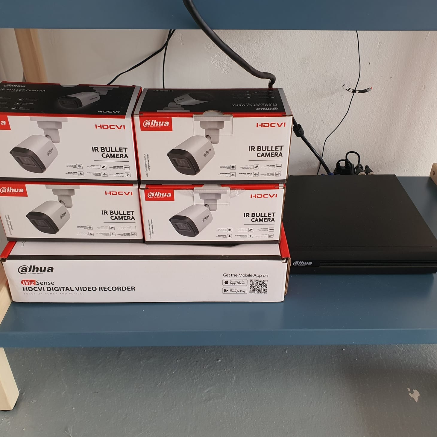 Four boxed Dahua HDCVI bullet cameras stacked beside a boxed Dahua WizSense recorder on a shelf.