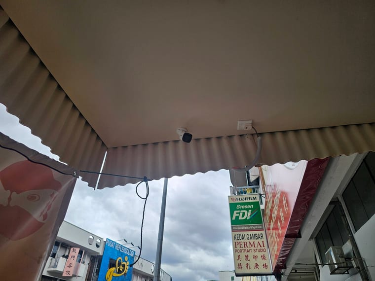 A camera fixed under a corrugated shop awning, seen from below against an overcast sky.
