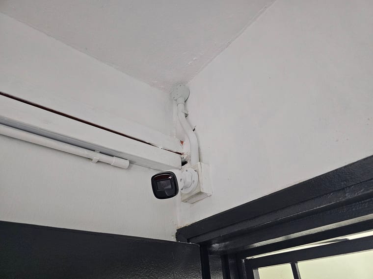 A bullet camera on a beam above a glass shop frontage, with conduit running along the ceiling.