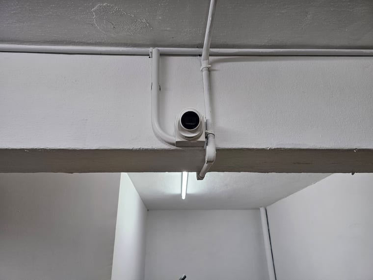 A surface conduit run along a white ceiling ending at a small camera in a corridor.