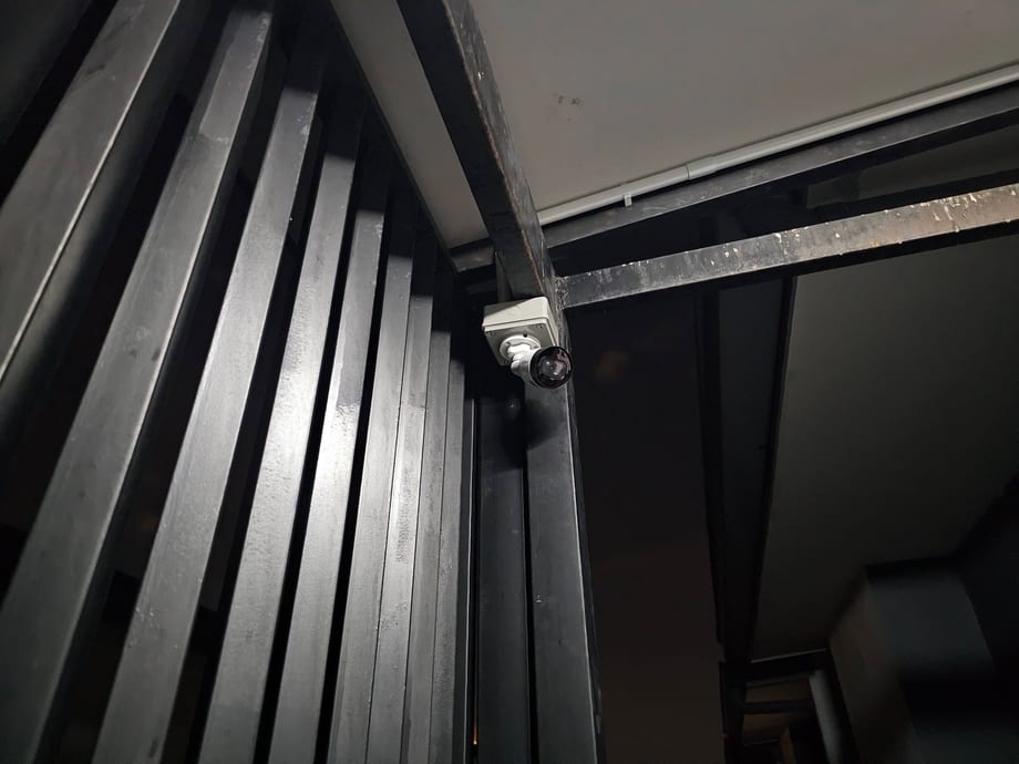 A camera mounted above a dark metal louvre gate.